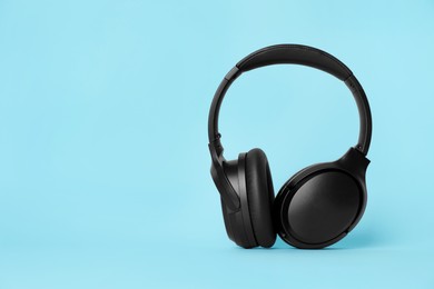 Photo of Modern wireless headphones on light blue background. Space for text
