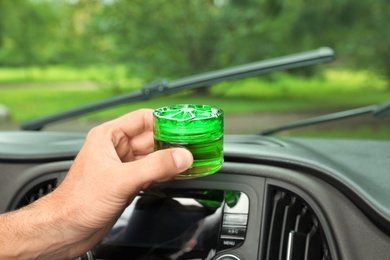 Photo of Man putting air freshener on dashboard in car, closeup