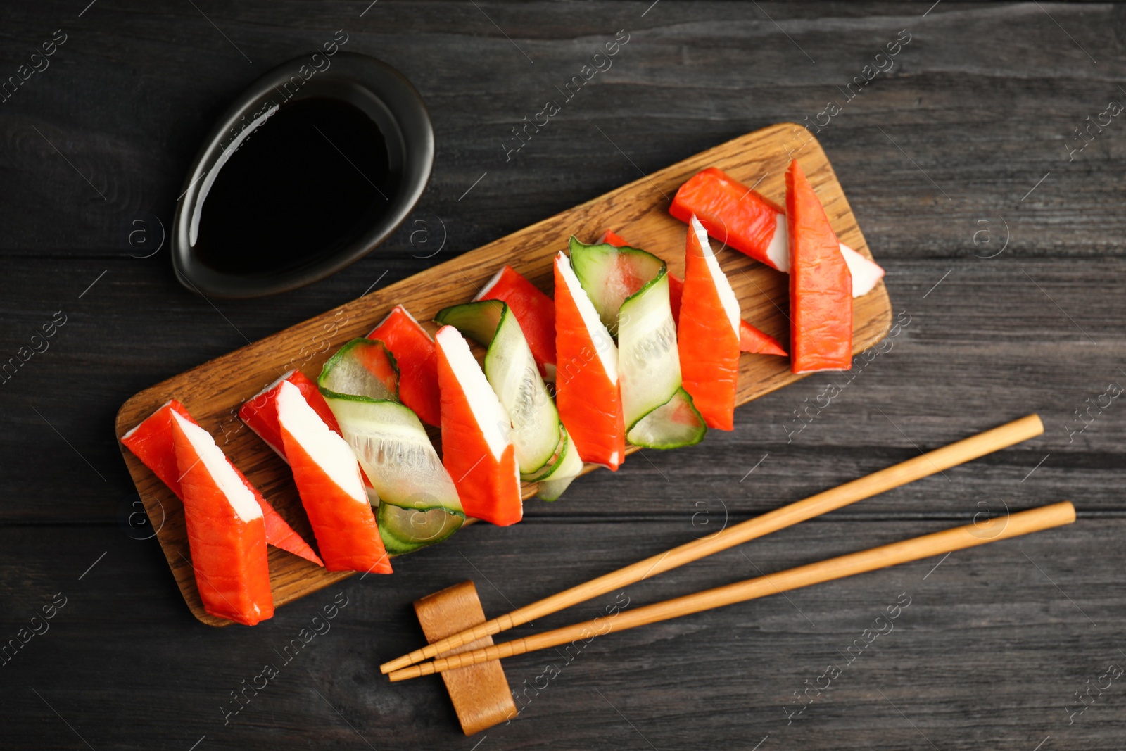 Photo of Crab sticks with cucumber and soy sauce served on dark wooden table, flat lay