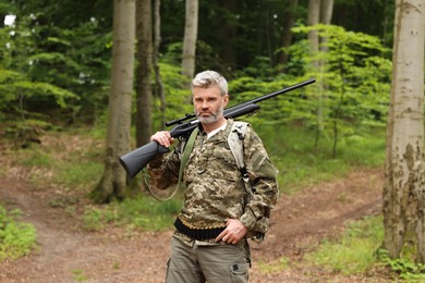 Photo of Man with hunting rifle and backpack wearing camouflage in forest