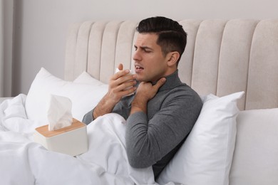 Sick man with box of paper tissues suffering from cold in bed at home