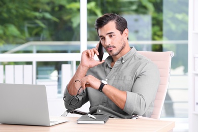 Handsome young man working with smartphone and laptop at table in office