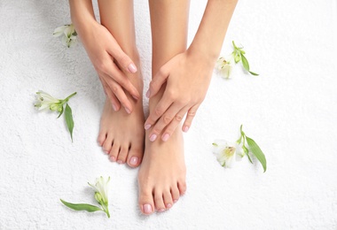 Photo of Woman touching her smooth feet on white towel, top view. Spa treatment