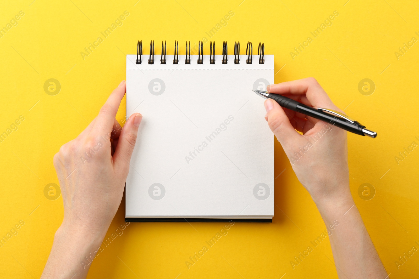 Photo of Woman writing in notebook on yellow background, top view