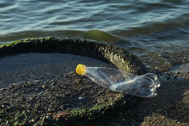 Photo of Plastic trash and tire on sand near water. Environment pollution