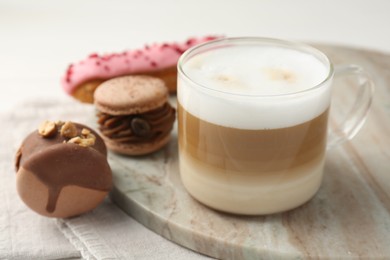 Photo of Aromatic coffee in cup, tasty macarons and eclair on table, closeup
