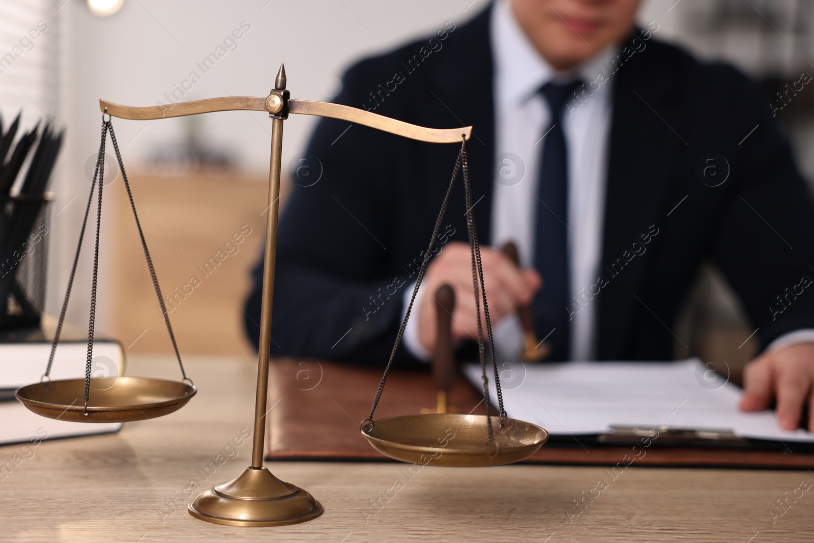 Photo of Notary stamping document at wooden table in office, focus on scales of justice