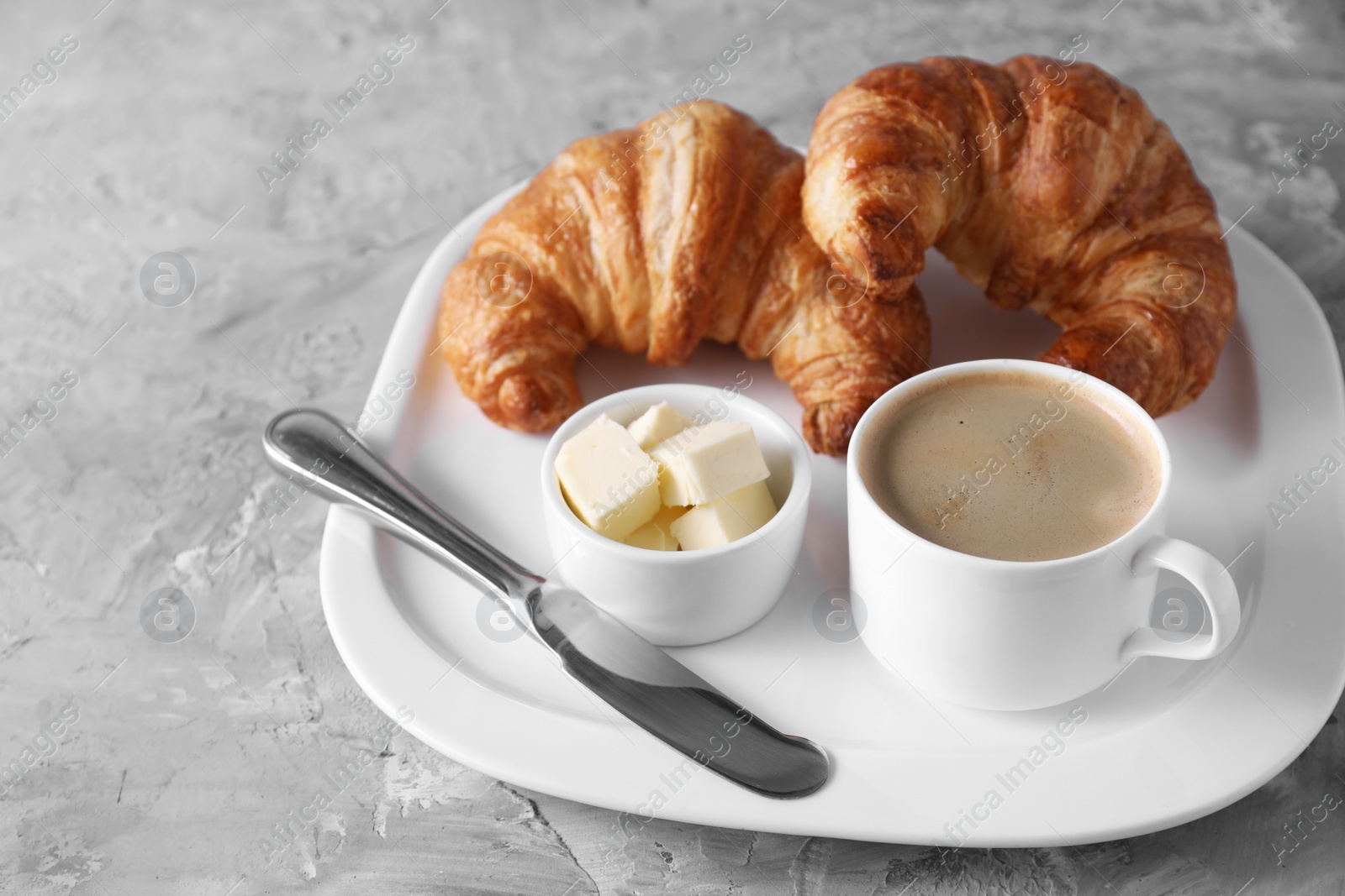 Photo of Tasty breakfast. Cup of coffee, fresh croissants, knife and butter on grey table, closeup