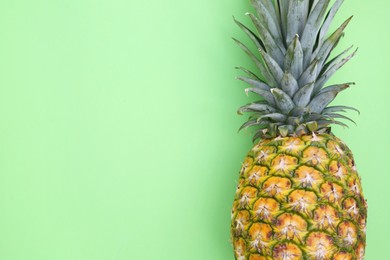 Whole ripe pineapple on light green background, top view. Space for text