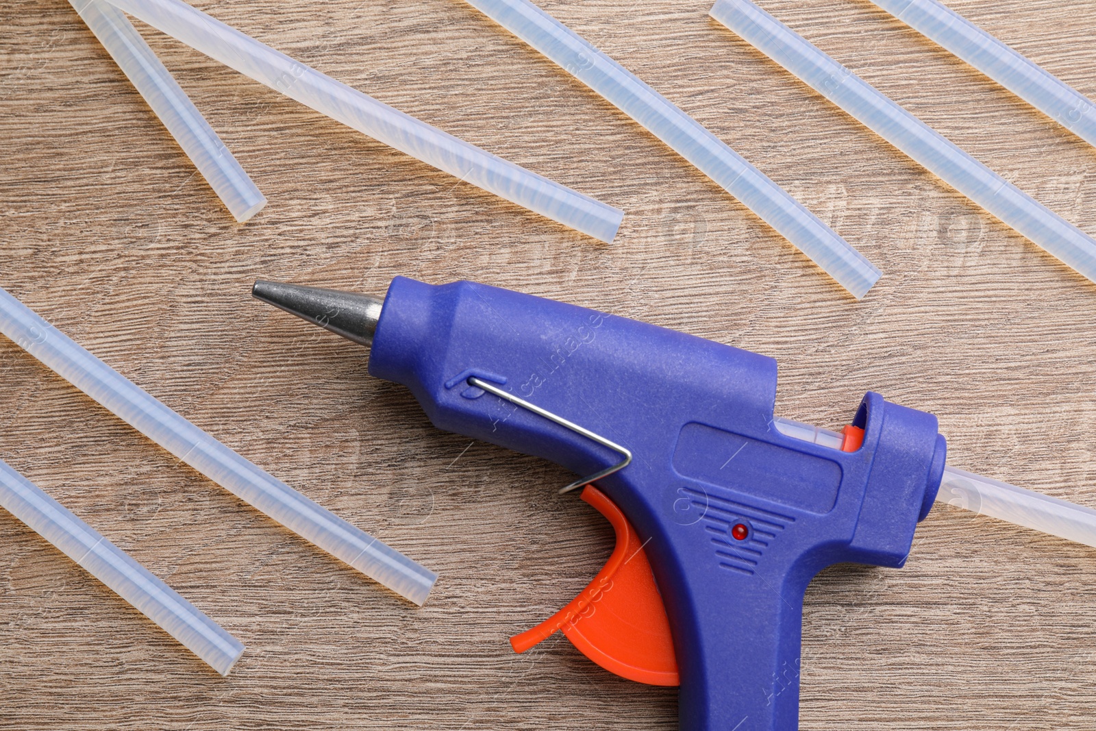 Photo of Dark blue glue gun and sticks on wooden table, flat lay