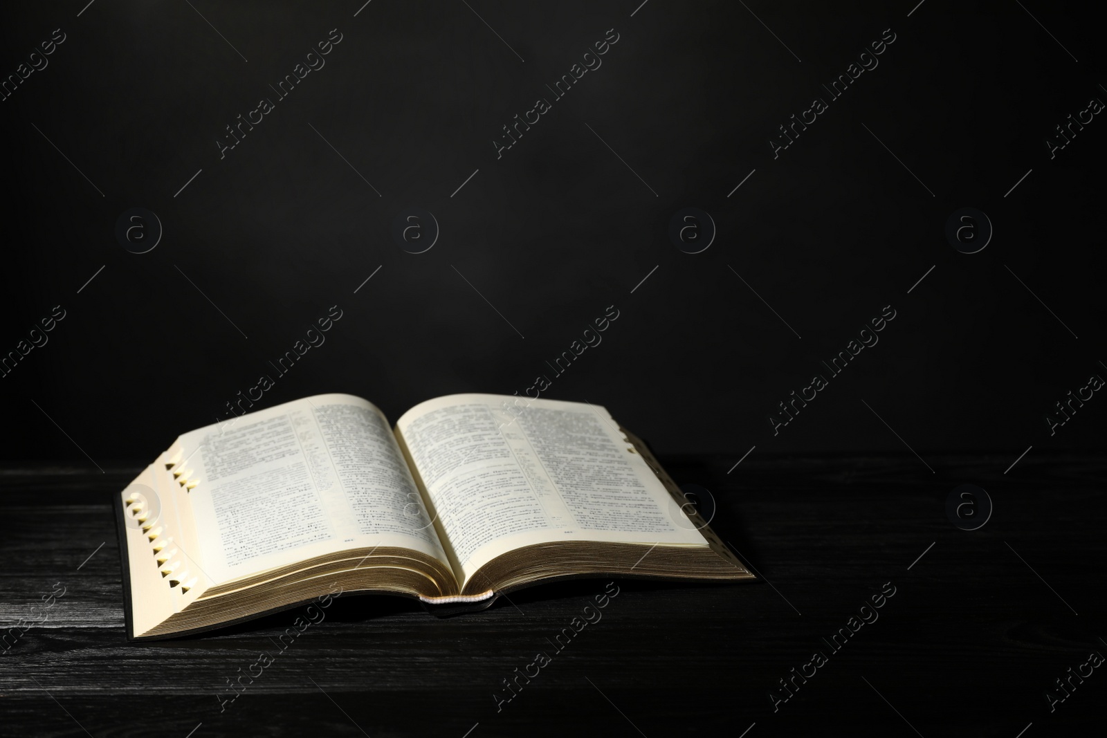 Photo of Open Bible on black wooden table, space for text. Christian religious book