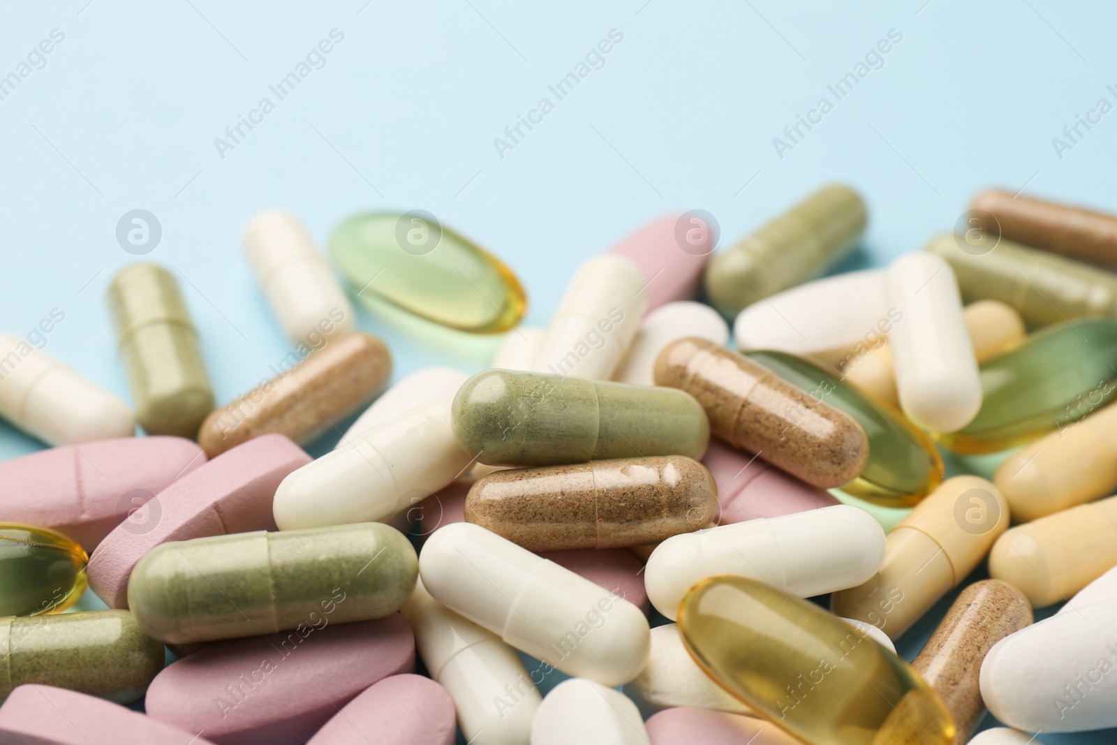 Photo of Different vitamin pills on light blue background, closeup