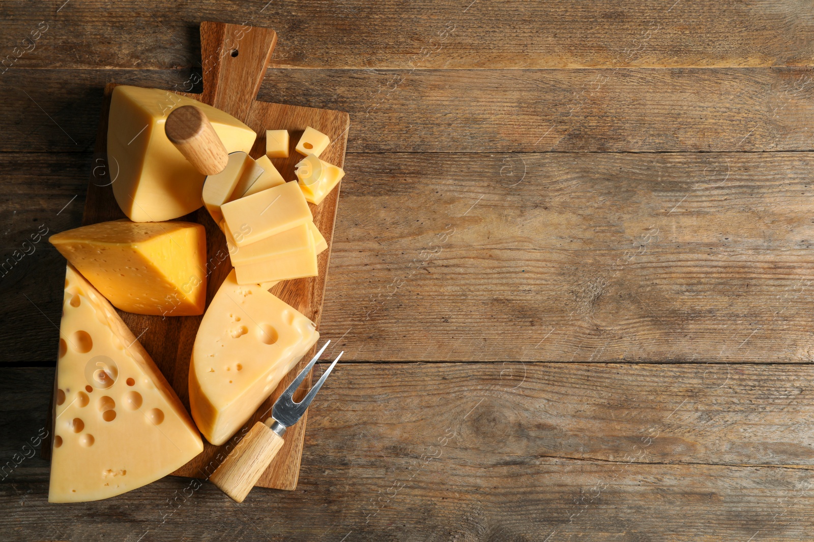 Photo of Different sorts of cheese, fork and knife on wooden table, top view. Space for text