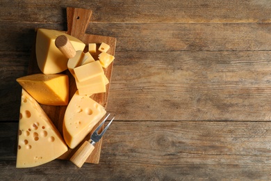 Different sorts of cheese, fork and knife on wooden table, top view. Space for text