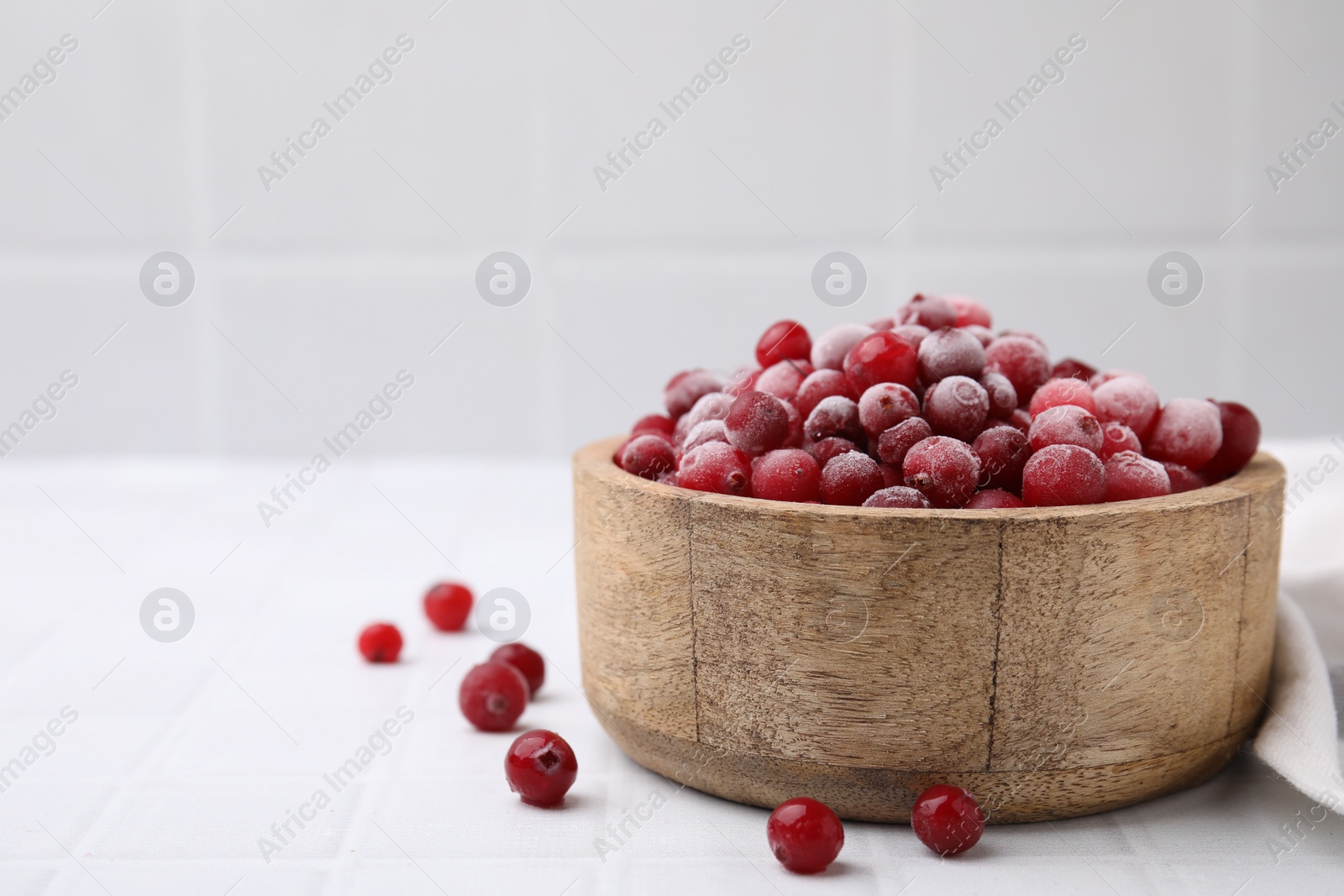 Photo of Frozen red cranberries in bowl on white tiled table, closeup. Space for text