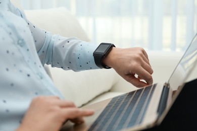 Mature woman with smart watch working on laptop indoors, closeup