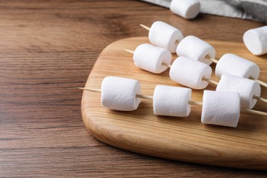 Photo of Sticks with delicious puffy marshmallows on wooden table. Space for text