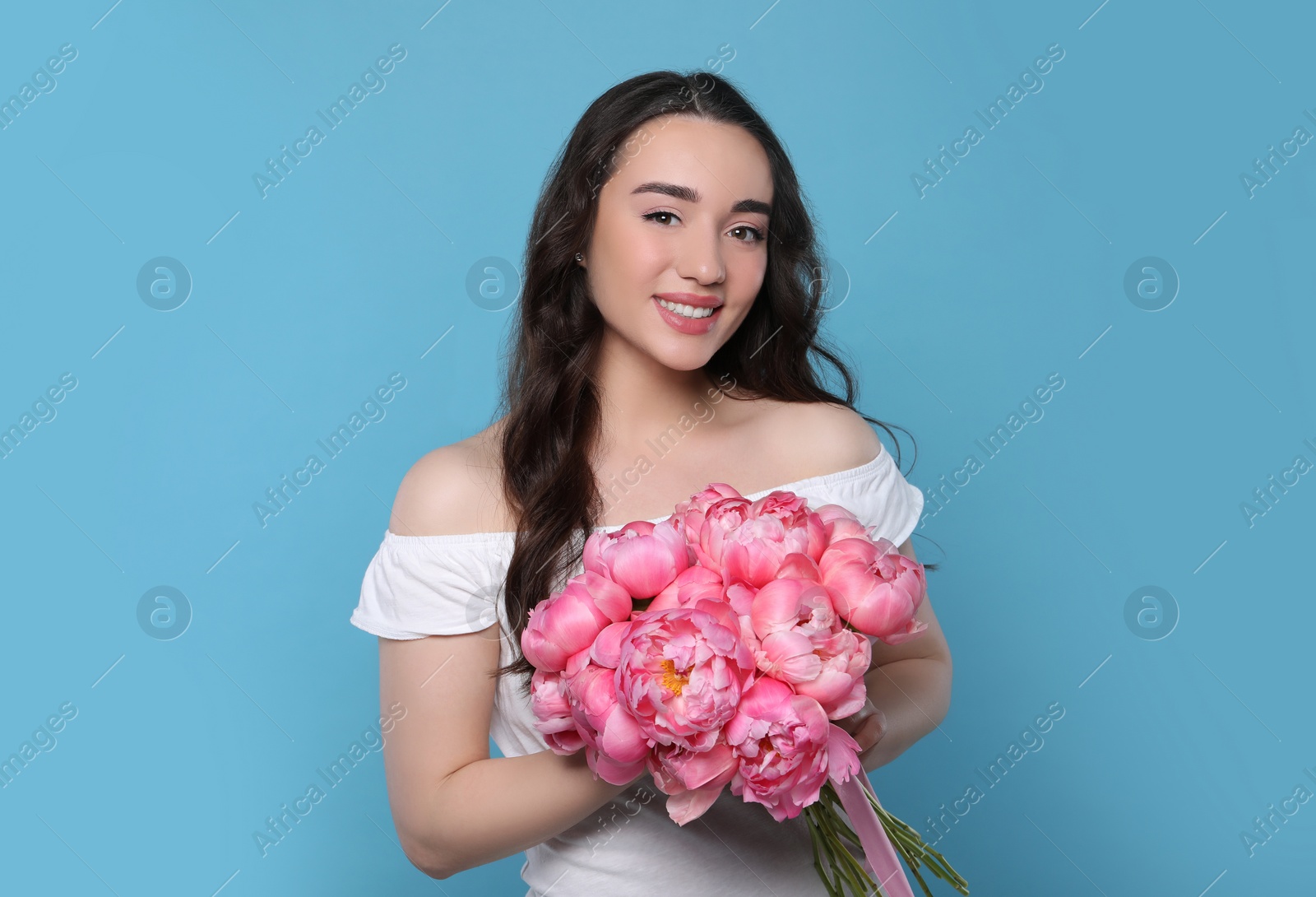 Photo of Beautiful young woman with bouquet of pink peonies on light blue background