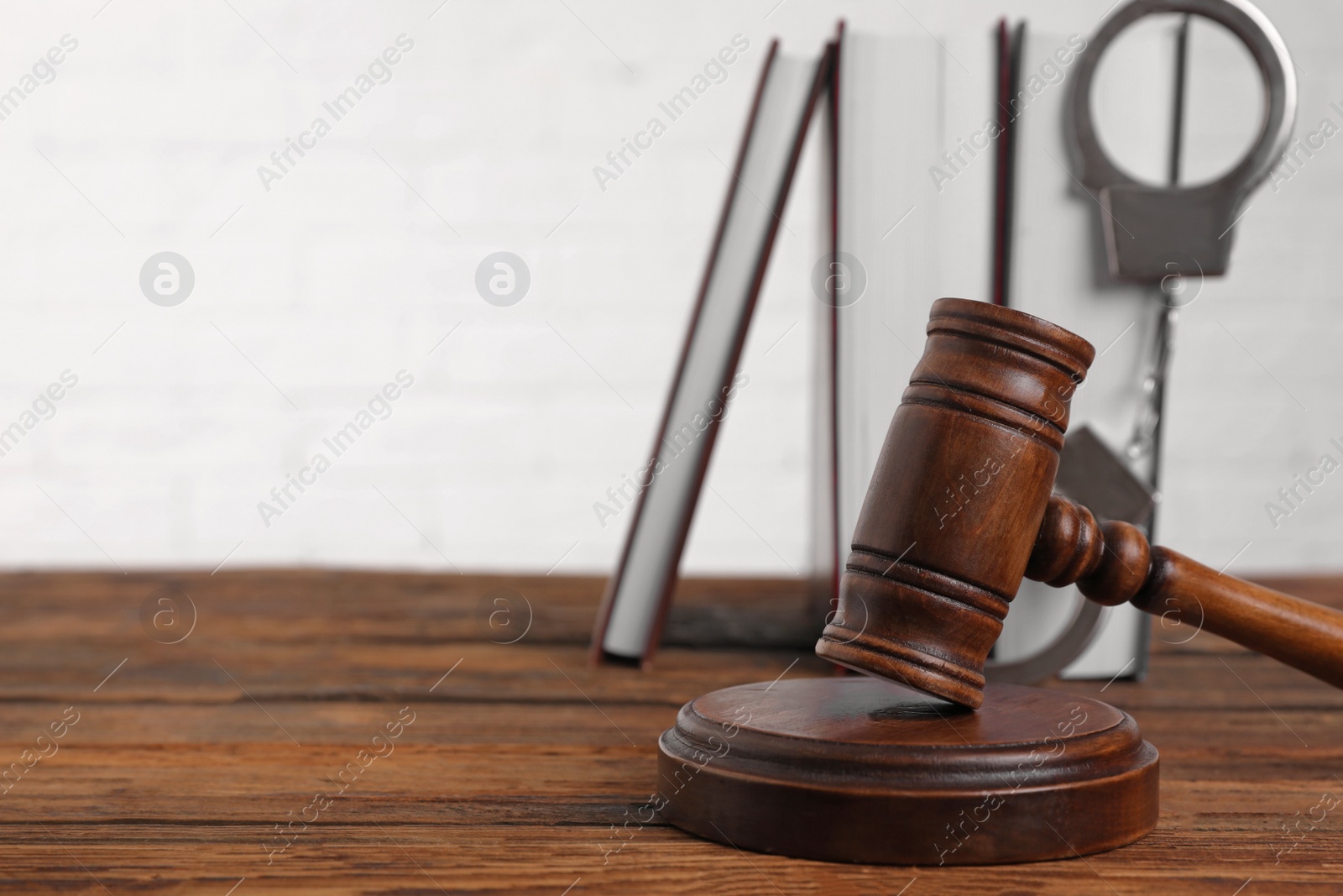 Photo of Gavel, handcuffs and book on wooden table, space for text. Criminal law