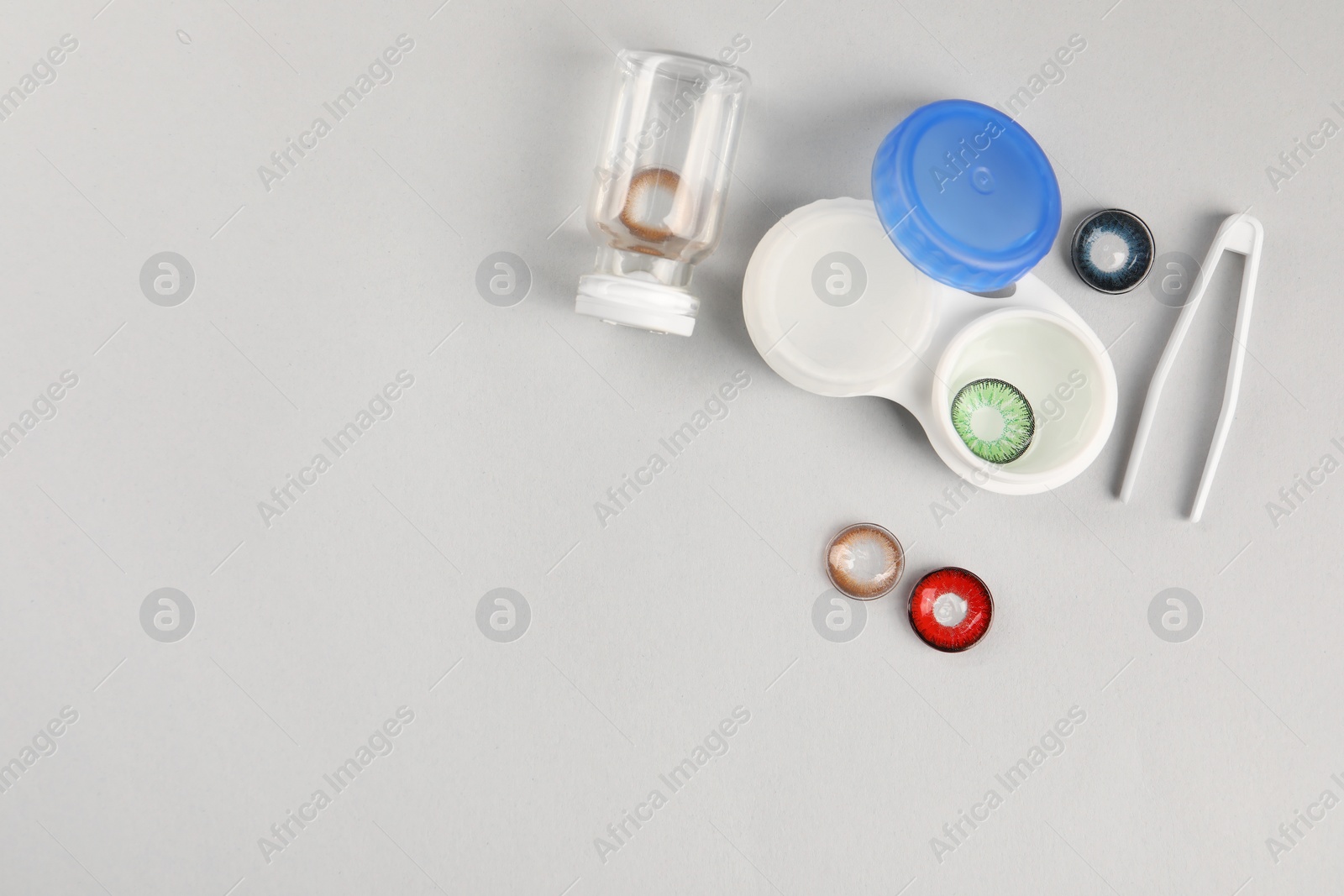 Photo of Different color contact lenses, tweezers and containers on light background, flat lay. Space for text
