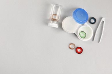 Photo of Different color contact lenses, tweezers and containers on light background, flat lay. Space for text