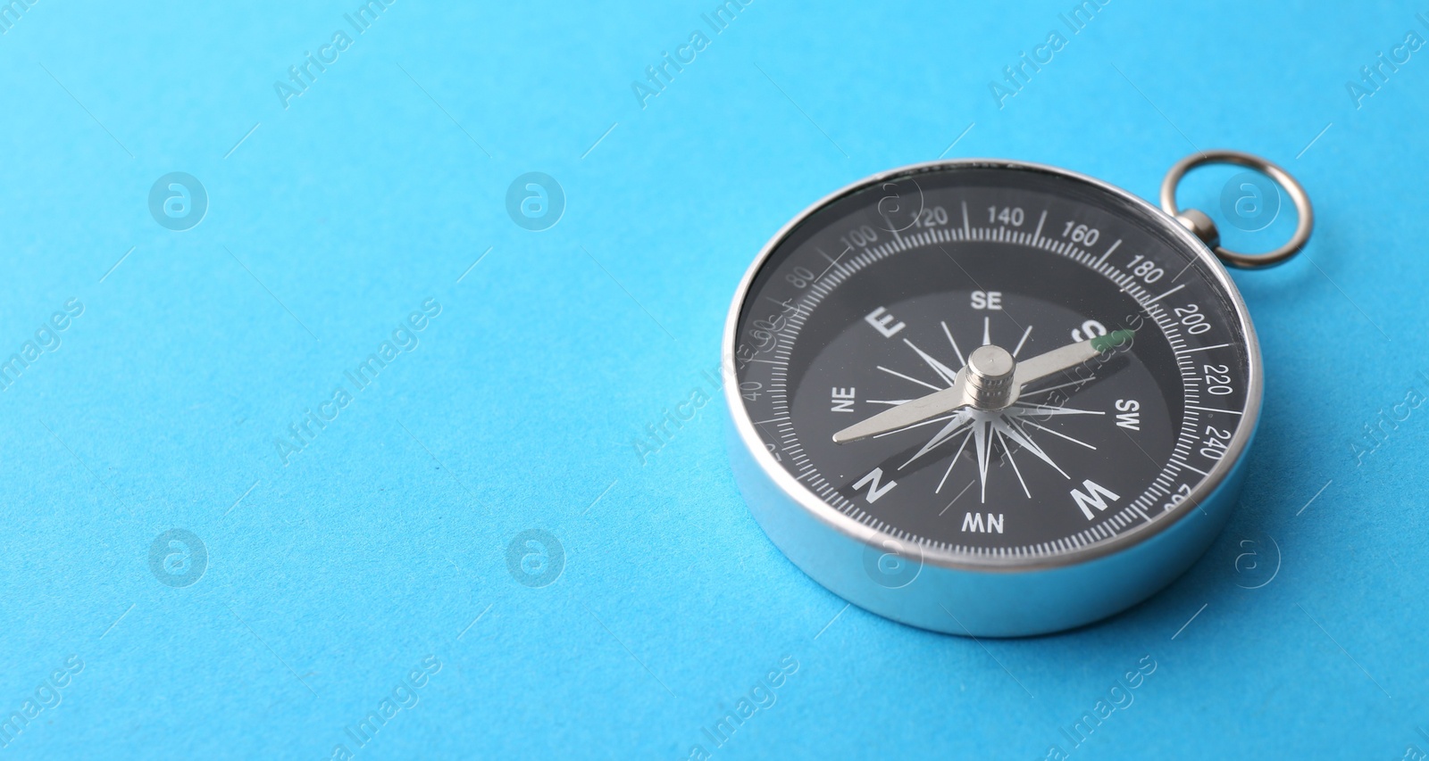 Photo of One compass on light blue background, closeup. Space for text
