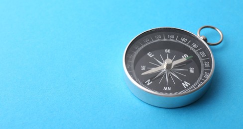 Photo of One compass on light blue background, closeup. Space for text