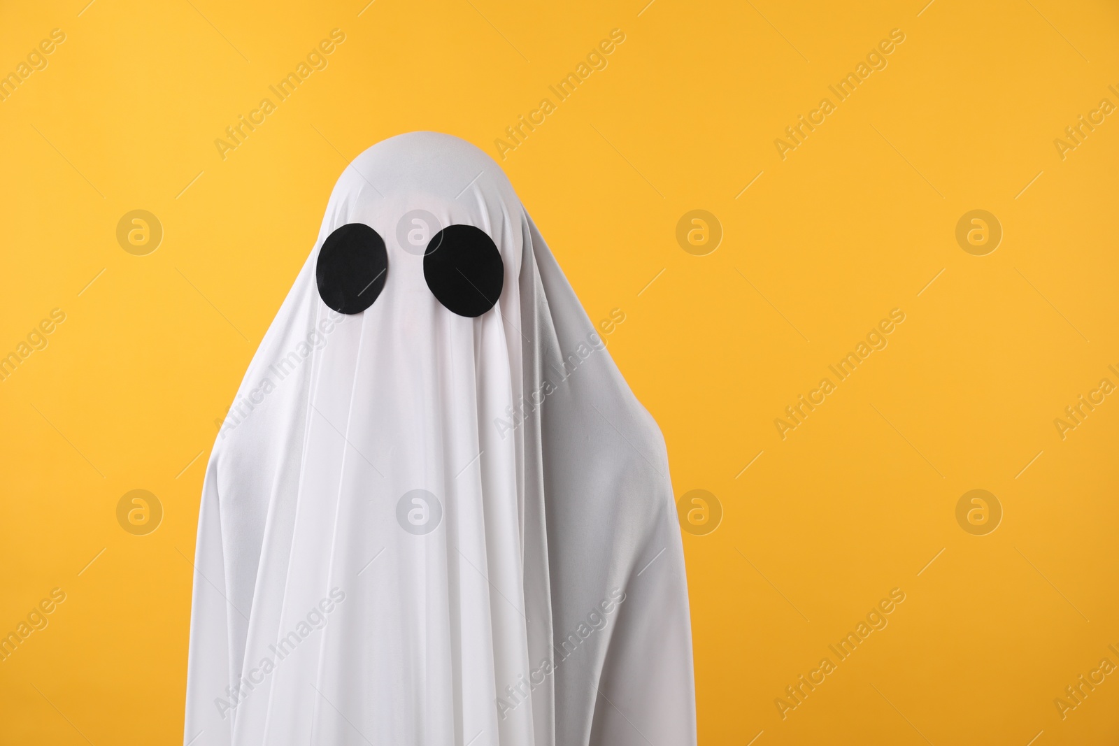 Photo of Creepy ghost. Person covered with white sheet on yellow background, space for text