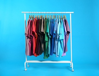 Photo of Colorful clothes hanging on rack against light blue background