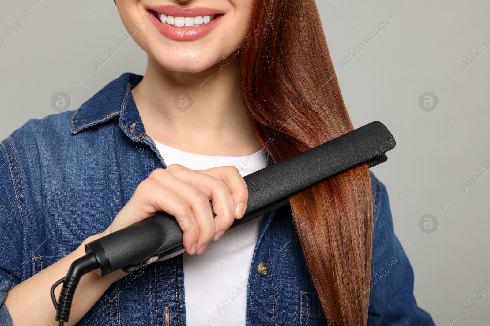 Photo of Woman using hair iron on light gray background, closeup
