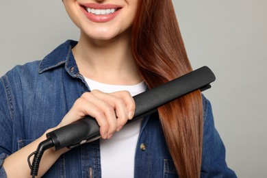 Woman using hair iron on light gray background, closeup