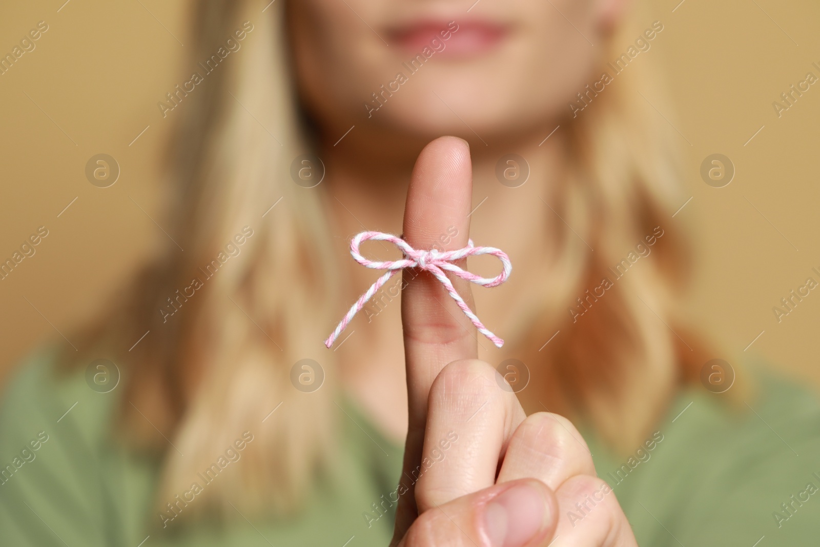 Photo of Woman showing index finger with tied bow as reminder against light brown background, focus on hand