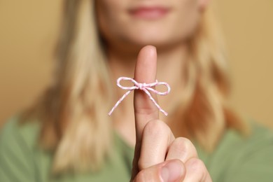 Woman showing index finger with tied bow as reminder against light brown background, focus on hand