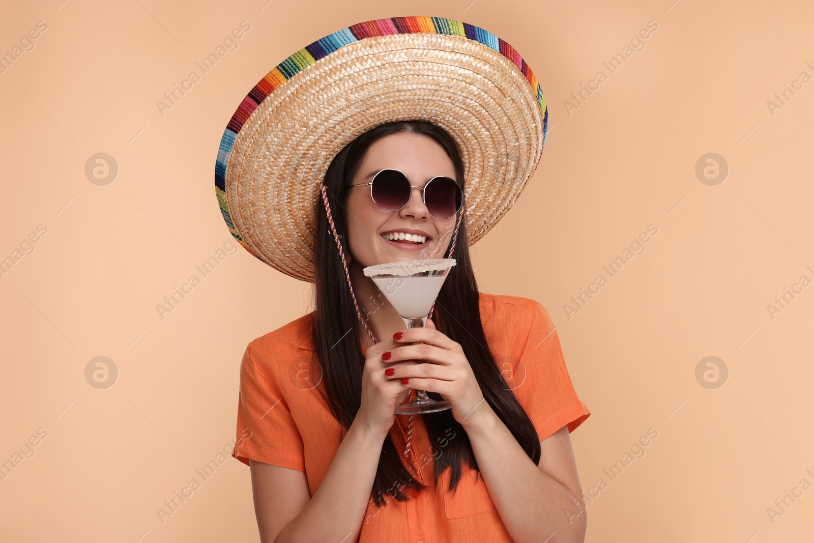 Photo of Young woman in Mexican sombrero hat with cocktail on beige background