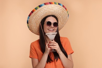 Young woman in Mexican sombrero hat with cocktail on beige background