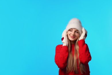 Portrait of emotional young woman in stylish hat, sweater and mittens on color background, space for text. Winter atmosphere