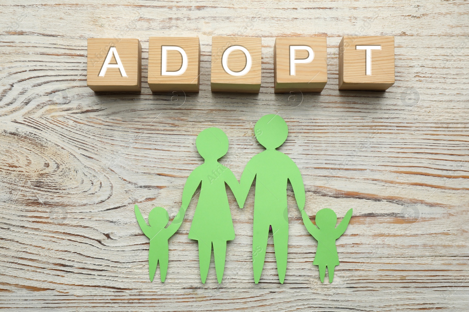 Photo of Family figure and word Adopt made of cubes on white wooden table, flat lay