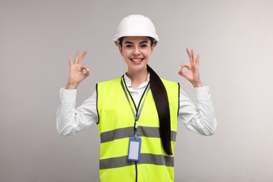 Photo of Engineer with hard hat and badge showing ok gesture on grey background