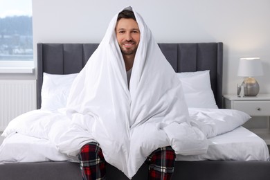 Photo of Happy man wrapped in blanket on soft bed at home in morning