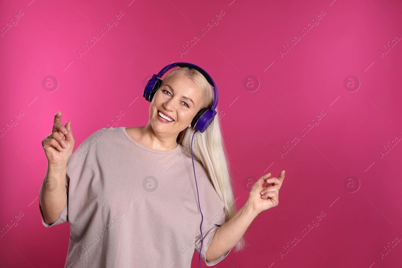 Photo of Mature woman enjoying music in headphones on color background. Space for text