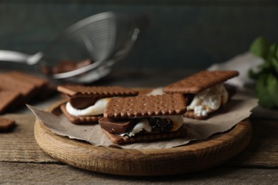 Photo of Delicious marshmallow sandwiches with crackers and chocolate on wooden table, closeup