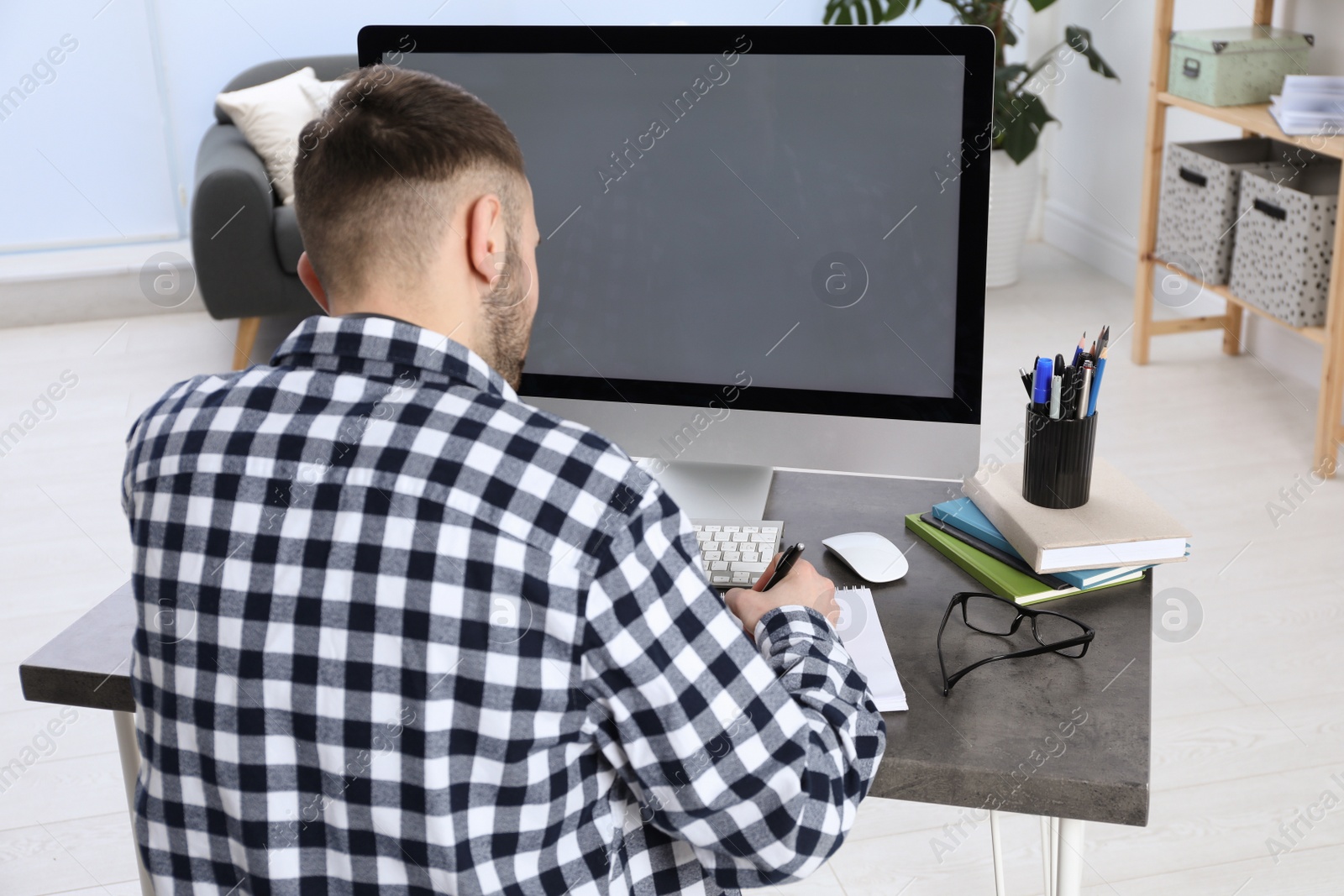 Photo of Young man using modern computer for studying at home, back view. Distance learning