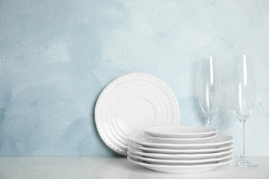 Set of clean plates and glasses on table against light blue background. Space for text