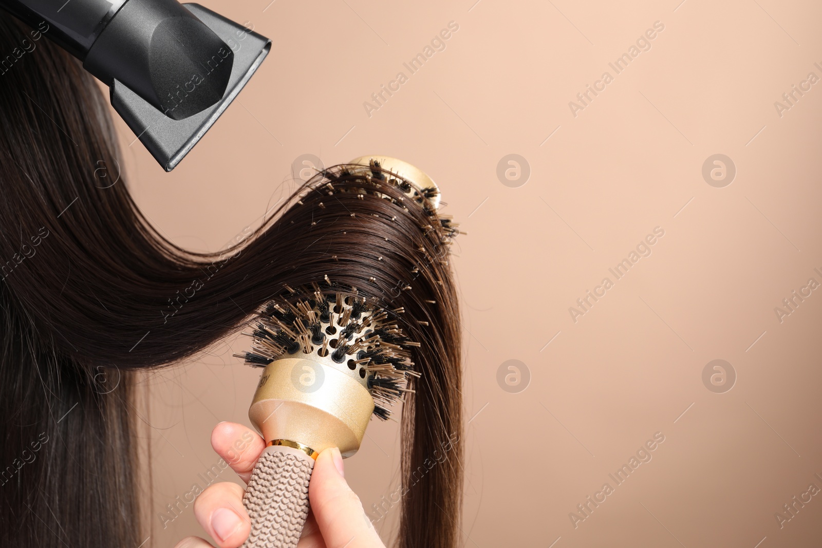 Photo of Hairdresser blow drying client's hair on beige background, closeup. Space for text