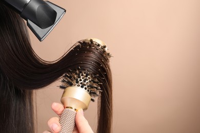 Photo of Hairdresser blow drying client's hair on beige background, closeup. Space for text