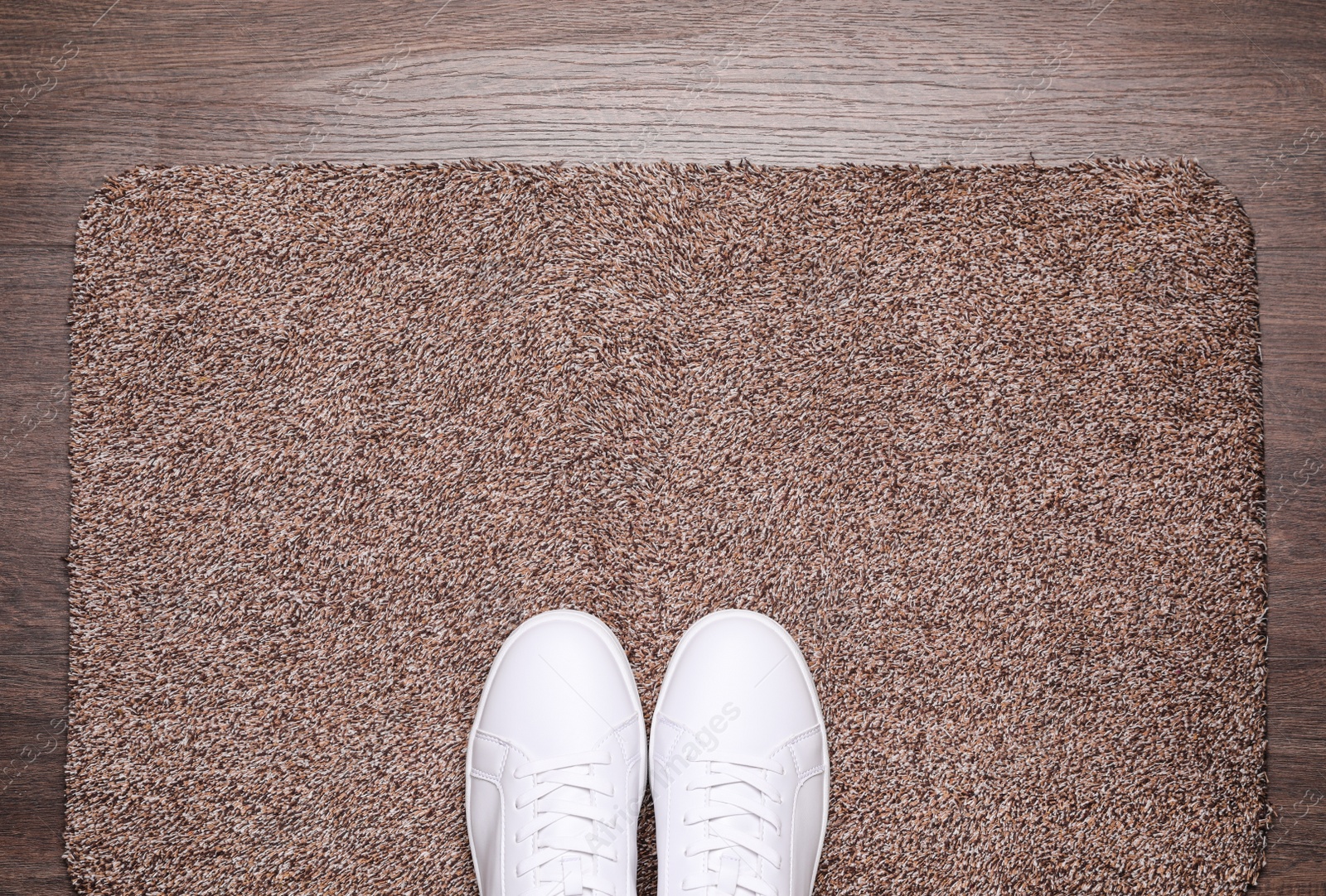 Photo of Stylish door mat and shoes on wooden floor, top view