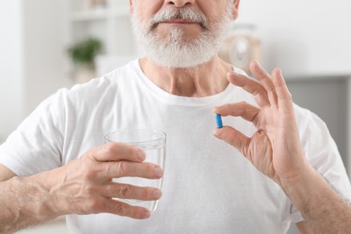 Photo of Senior man with glass of water and pill at home, closeup