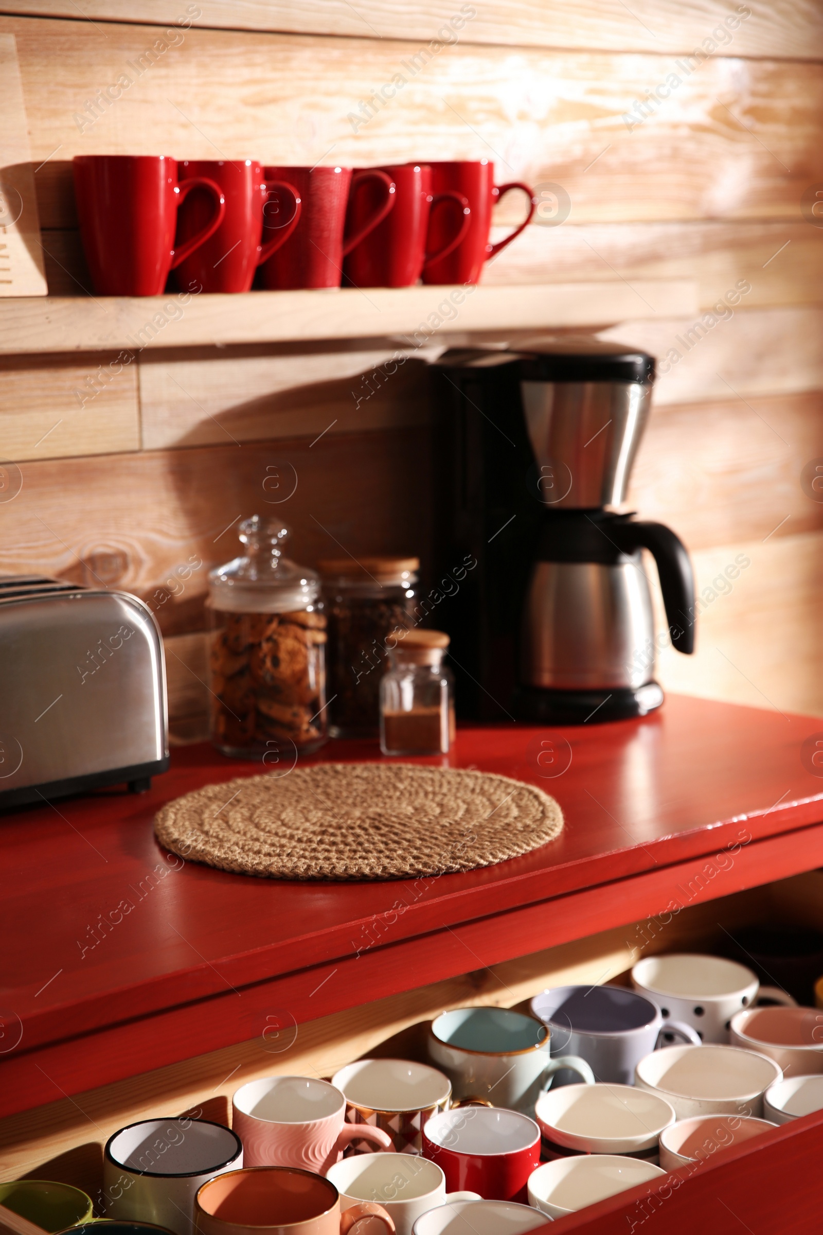 Photo of Open drawer with cups and coffeemaker near wooden wall indoors