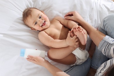 Photo of Mother with bottle of dusting powder near her cute baby on bed, top view