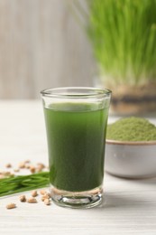 Photo of Wheat grass drink in shot glass on white wooden table, closeup